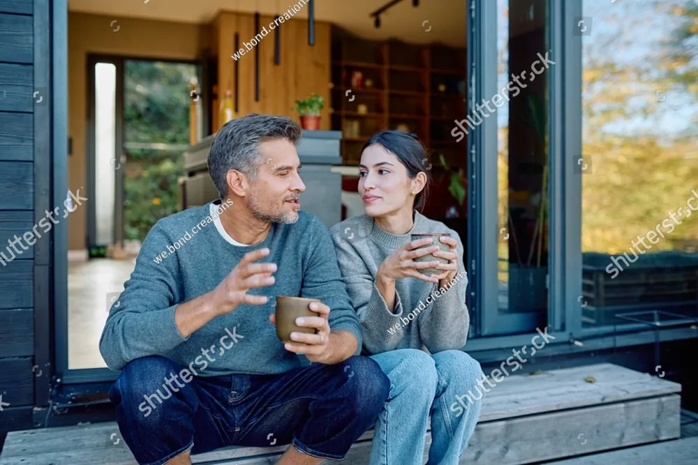 A smiling couple sitting together with coffee on their porch