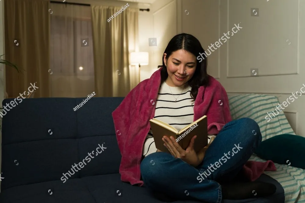 A woman smiling as she reads on the couch