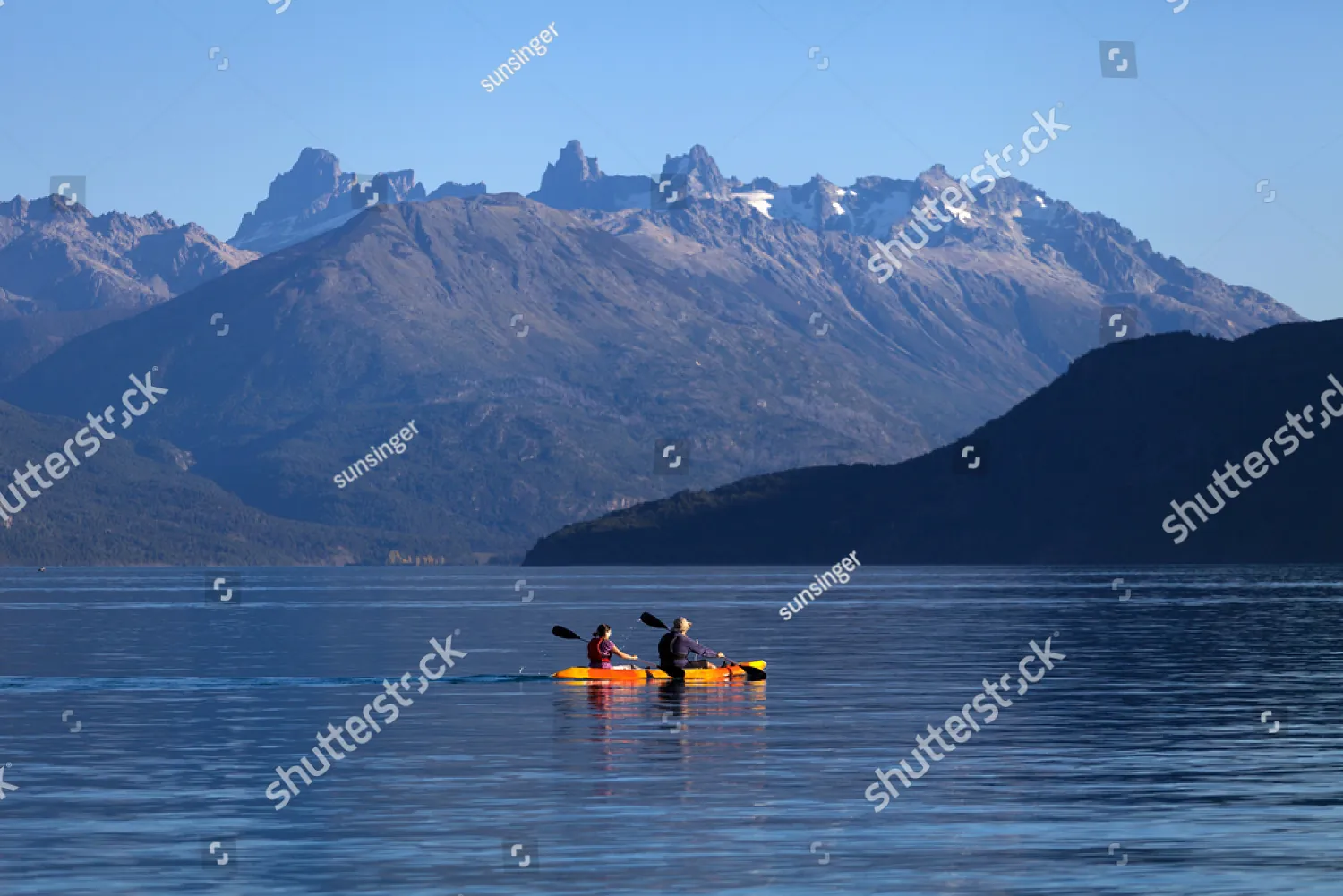Two people paddling a kayak below jagged mountains