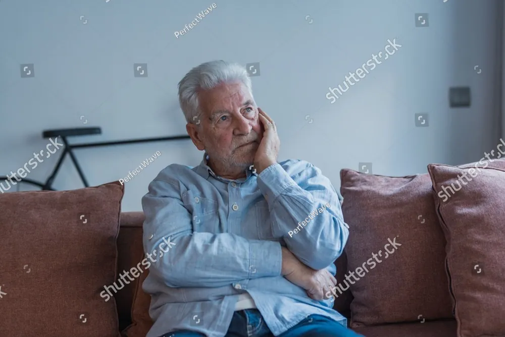 An older man sitting alone on his couch, lost in thought