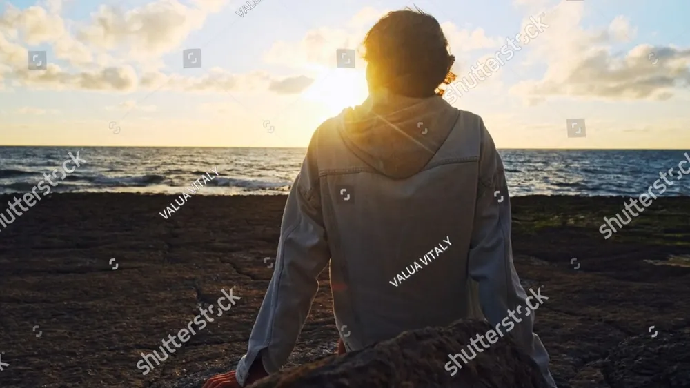 A woman sitting on a beach watching the sun set over the sea