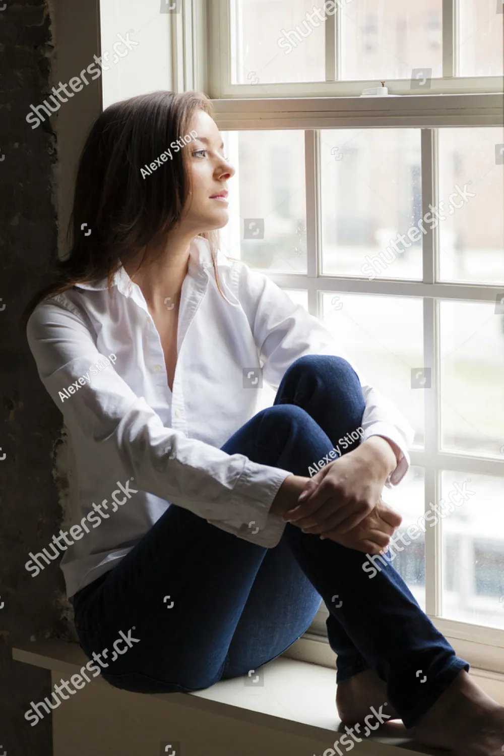 A woman sitting on a sunlit window seat, looking outside
