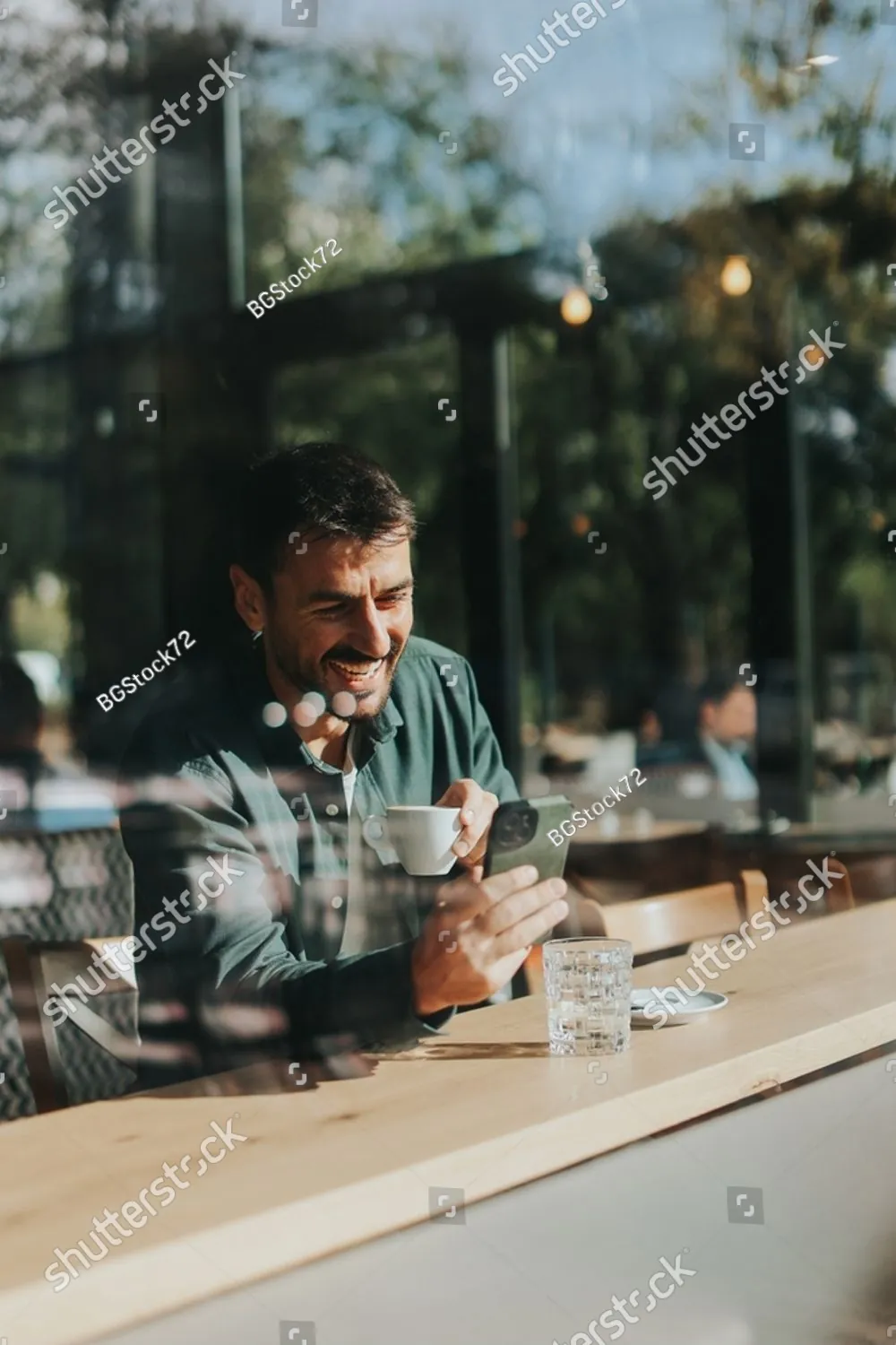 A man smiling over coffee at a sunny cafe table