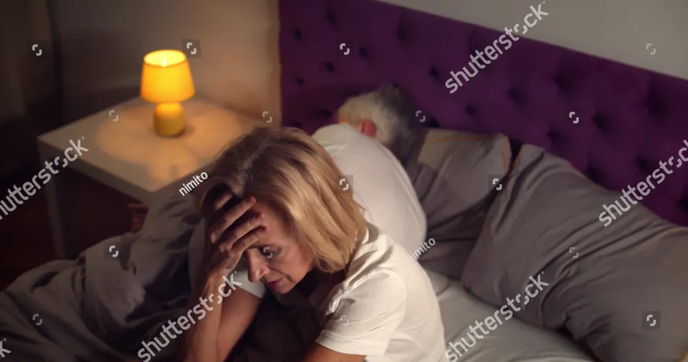 A woman awake in bed, her head in her hand, beside a lamp