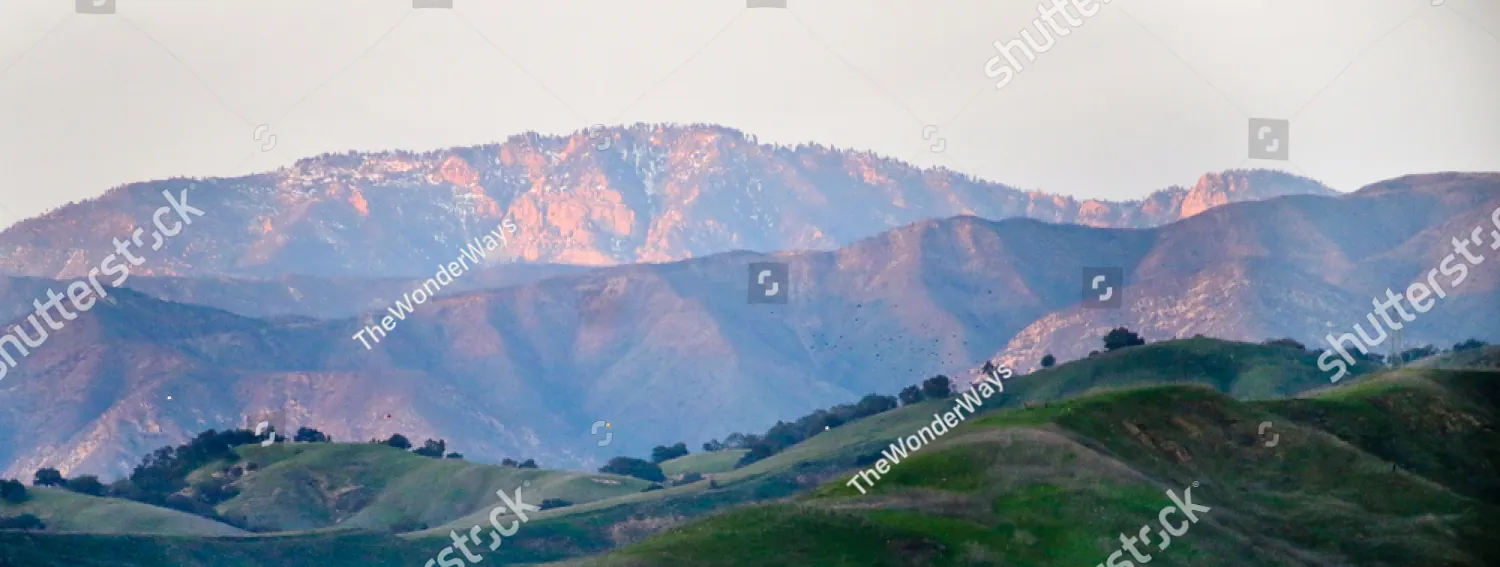Morning light on green hills below a mountain ridge